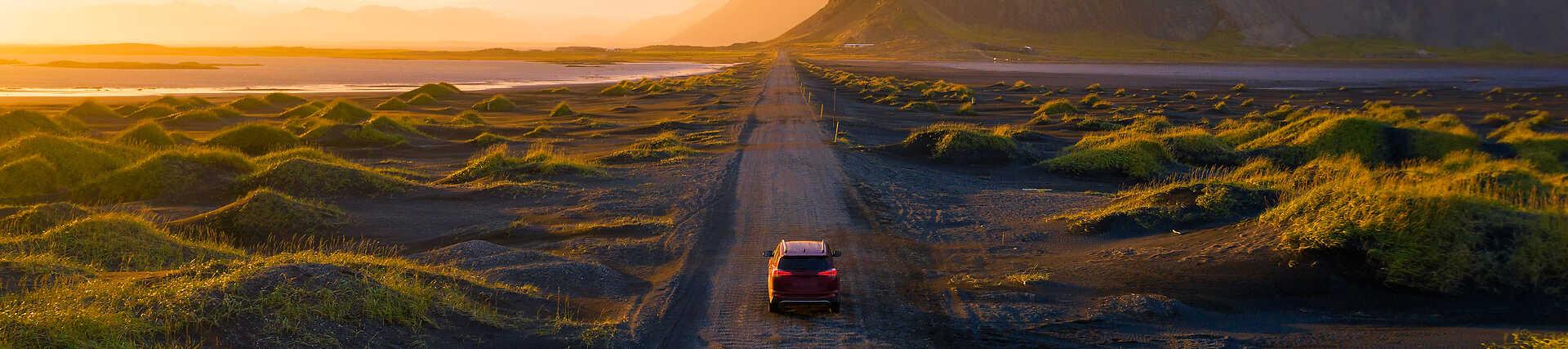 Mietwagen auf Schotterstraße vor Berglandschaft in Island.