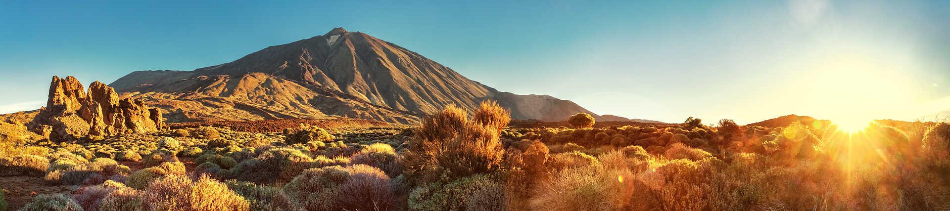 Majestätischer Teide-Vulkan auf Teneriffa, umgeben von trockener Landschaft unter blauem Himmel.