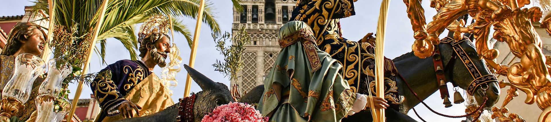 Detailaufnahme des goldenen Paso der Bruderschaft La Borriquita während der Osterprozession in Sevilla, mit La Giralda im Hintergrund und Palmenwedeln und Blumen geschmückt.