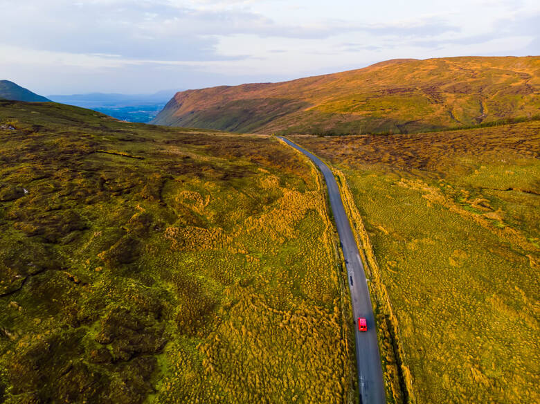 Rotes Auto fährt durch die irischen Berge in den Sonnenuntergang