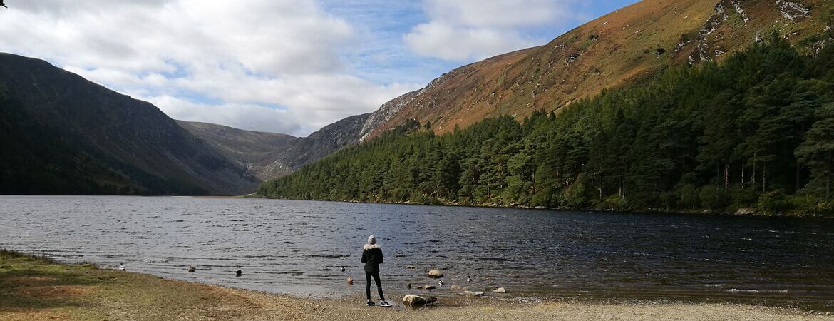 Frau blickt auf einen See im Wicklow Mountains National Park in Irland