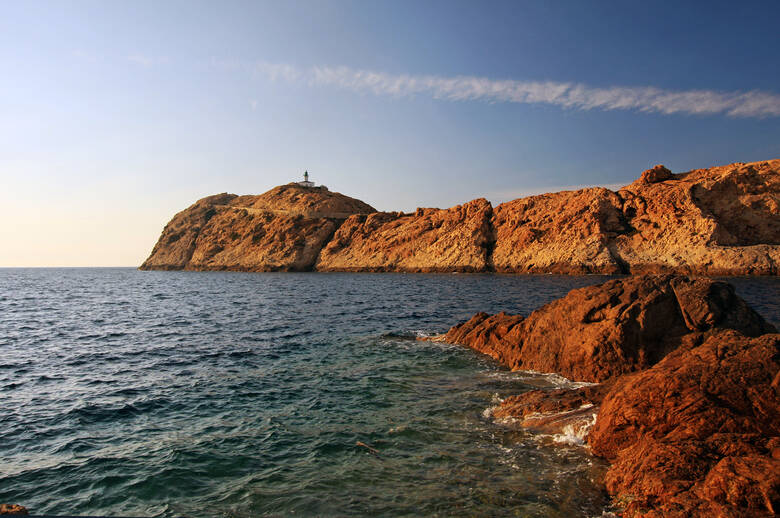 Rote Felsen, das Meer und ein Leuchtturm auf Sardinien