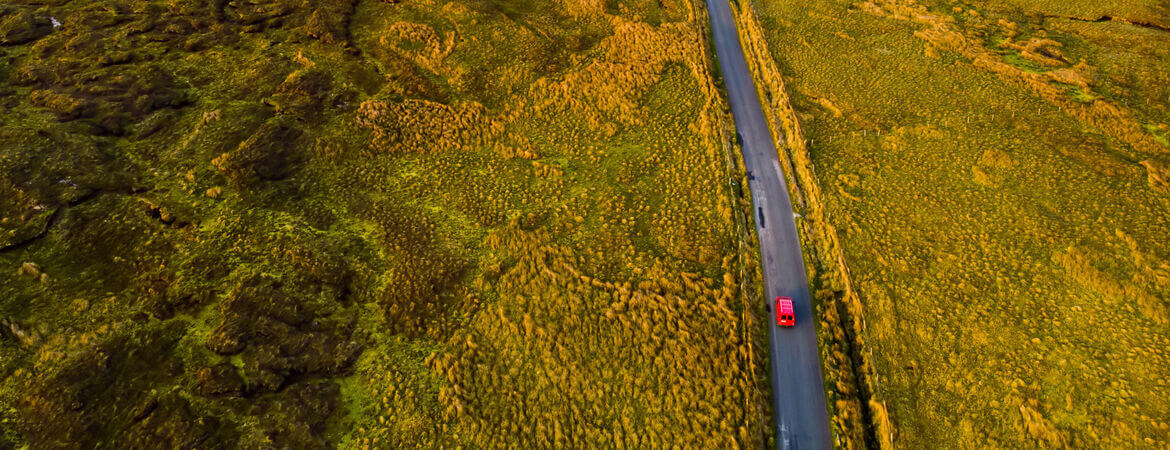 Rotes Auto fährt durch Hügellandschaft in Irland