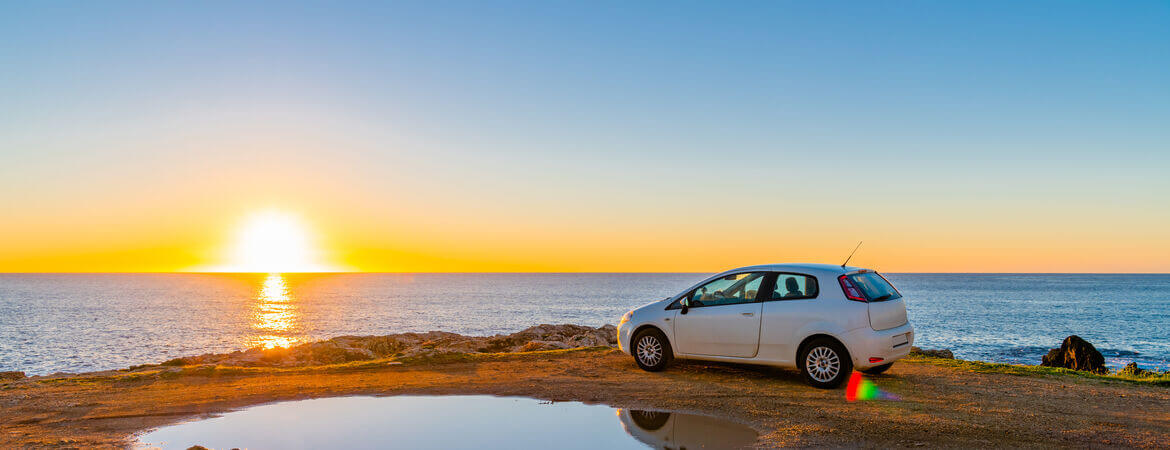 Auto steht am Meer auf Sizilien bei Sonnenuntergang