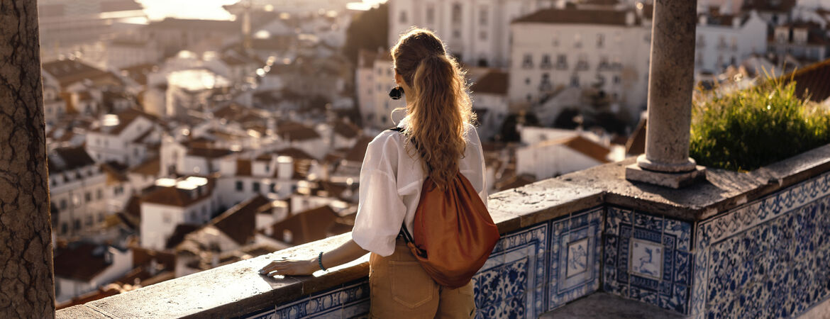 Frau schaut von Balkon in Lissabon auf die Altstadt