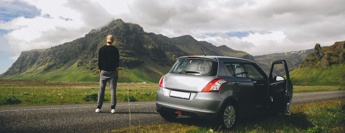Mann steht neben seinem Auto in Island und schaut auf die Berge