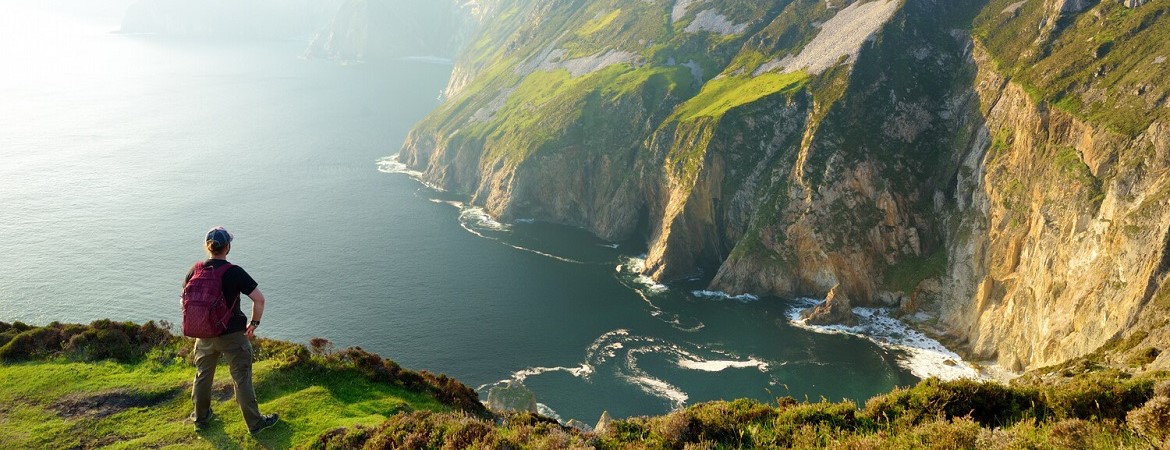 Mann steht an Klippen in Irland und schaut auf das Meer
