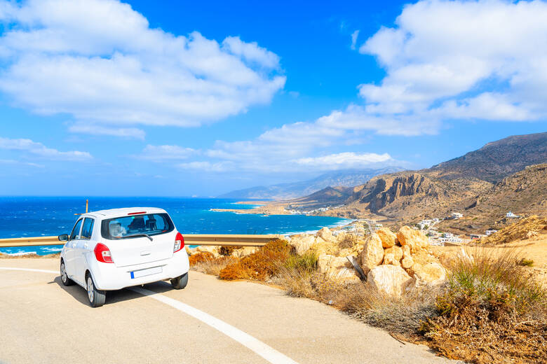 Weißes Auto fährt Küstenstraße in Griechenland entlang