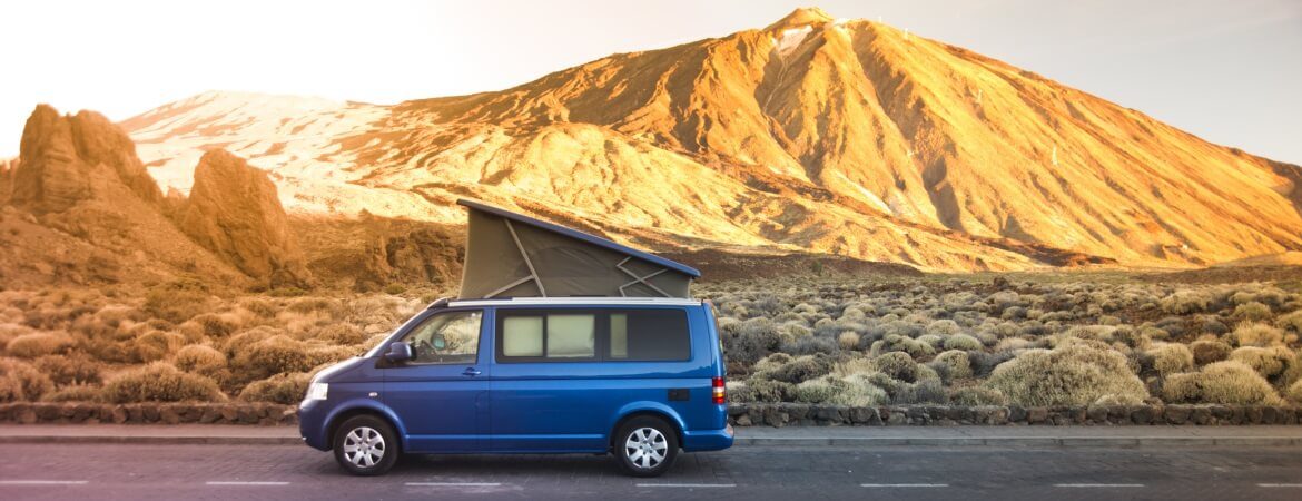 Blauer Minivan fährt Straße vor Bergkulisse entlang
