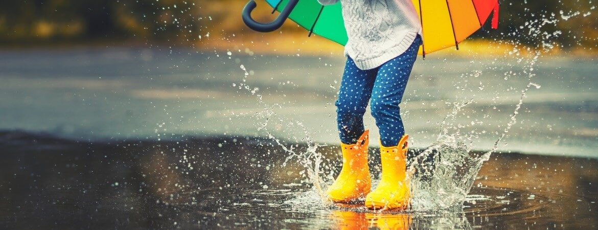 Kind mit gelben Gummistiefeln springt in Regenpfütze