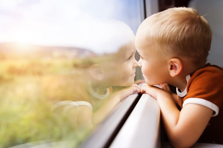 Kleiner Junge schaut aus dem Zugfenster auf die vorbeiziehende Landschaft