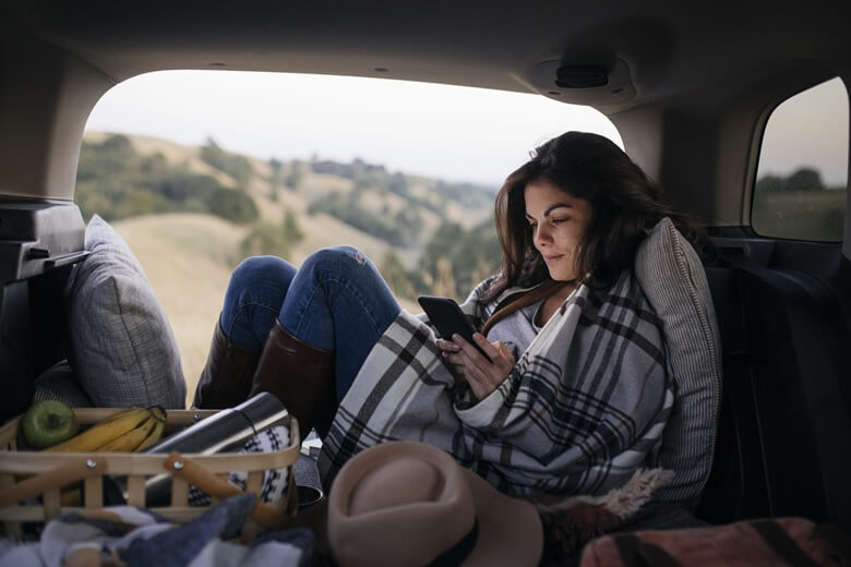 Frau sitzt mit Handy im Auto während einem Roadtrip