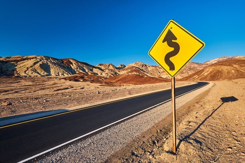 Ein Schild in der Wüste im Westen der USA zeigt eine kurvige Straße an