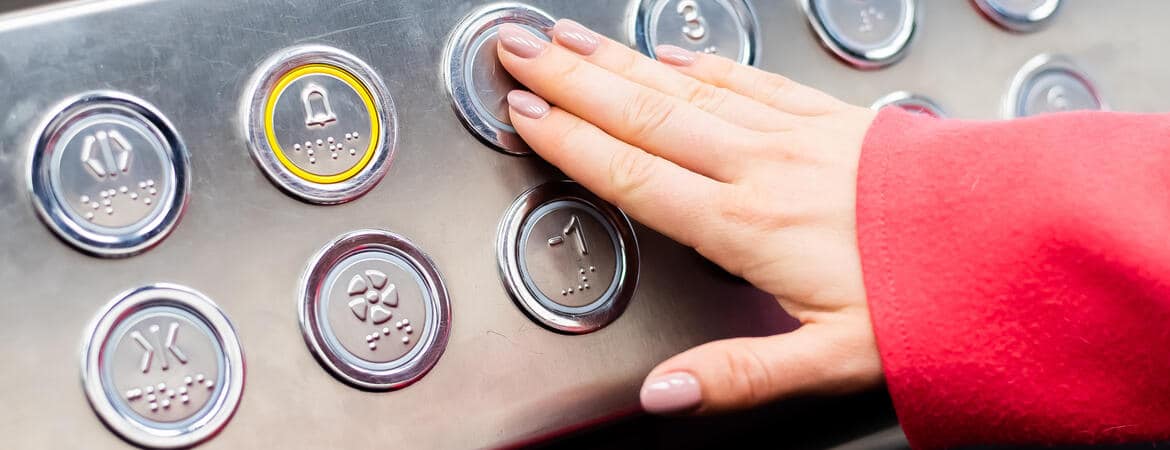 Frau drückt im Aufzug einen Knopf mit Braille-Schrift