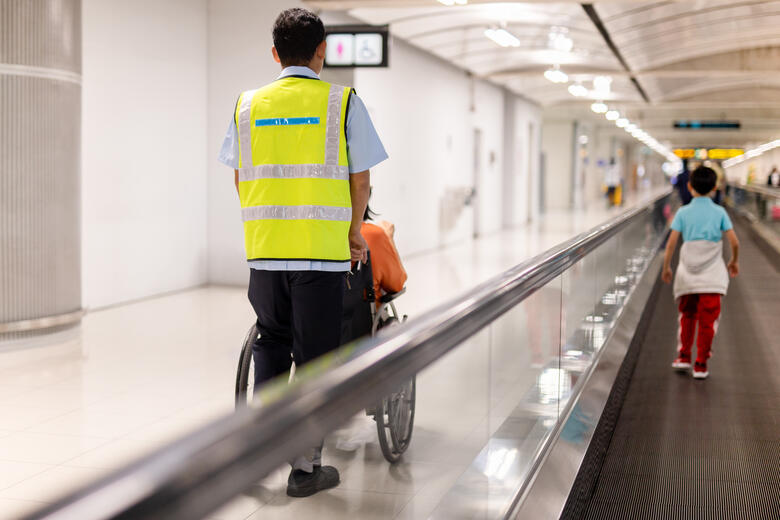 Frau im Rollstuhl erhält Hilfe im Flughafen-Terminal.