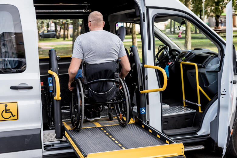 Mann im Rollstuhl wird mit einem Liftsystem in den Mietwagen gehoben.