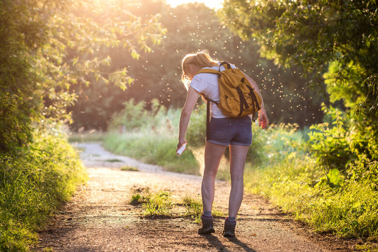 Eine Frau beim Wandern trägt Mückenspray auf