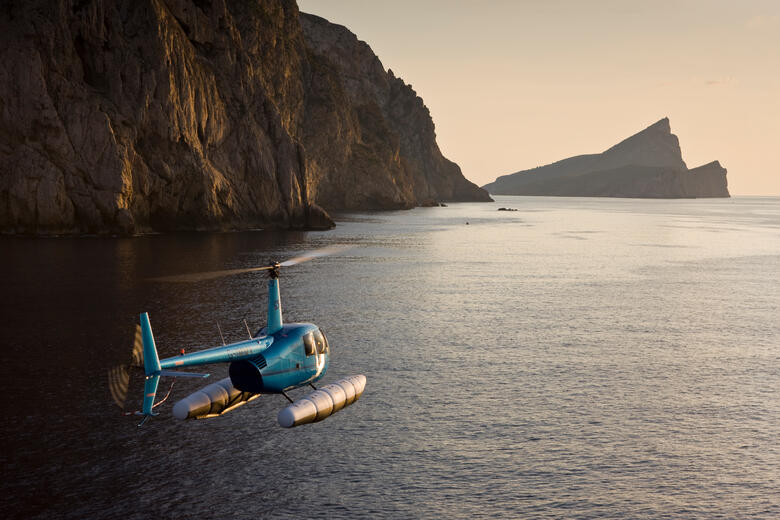 Helikopter fliegt im Abendlicht übers Meer an Mallorcas Küste