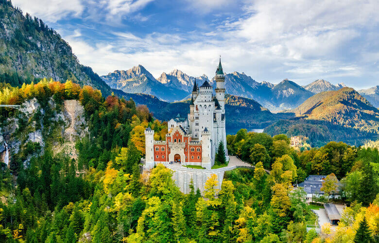 Schloss Neuschwanstein mit Wald und Alpen im Hintergrund