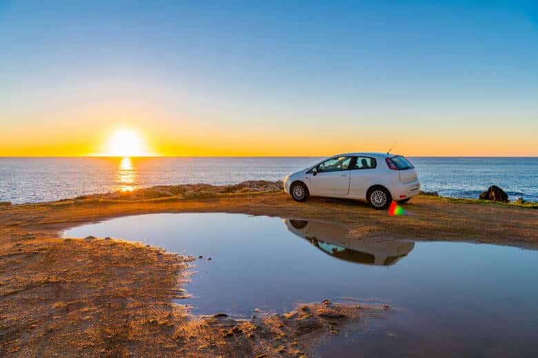 Auto steht bei Sonnenuntergang am Meer