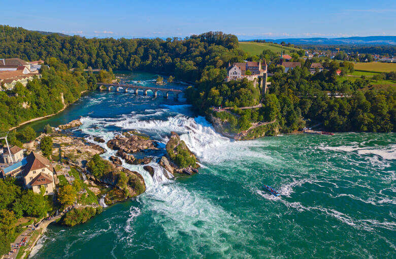 Eine Burg, eine Eisenbahnbrücke und der Rheinfall aus der Luft gesehen