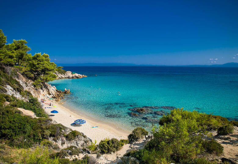 Ein kleiner Strandabschnitt mit Sonnenschirmen und blauem Wasser umgeben von Klippen und grün