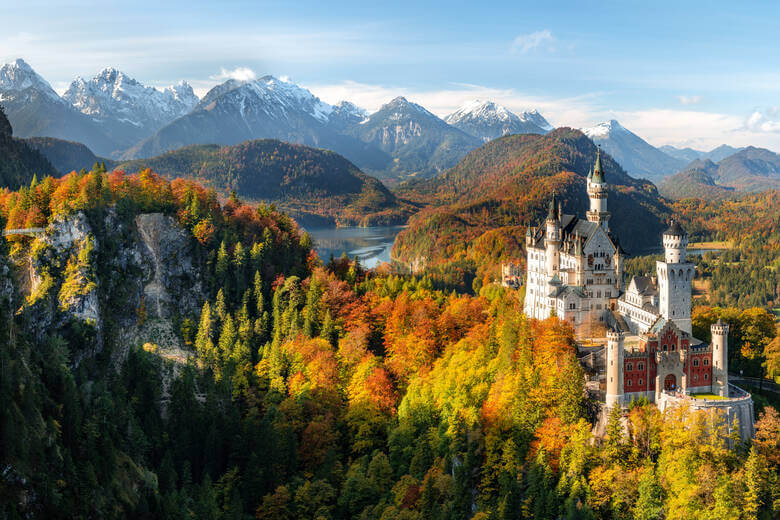 Schloss Neuschwanstein mit herbstlichem Wald und Alpen im Hintergrund