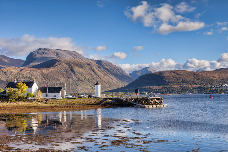 Fort William umgeben von Wasser mit Ausblick auf den Berg Ben Nevis, blauer Himmel