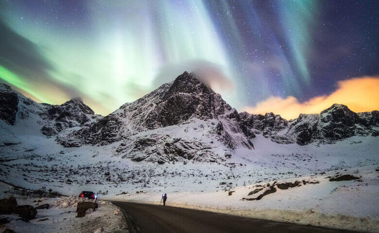 Fotograf steht vor Schneebergen in Norwegen und fotografiert die Polarlichter