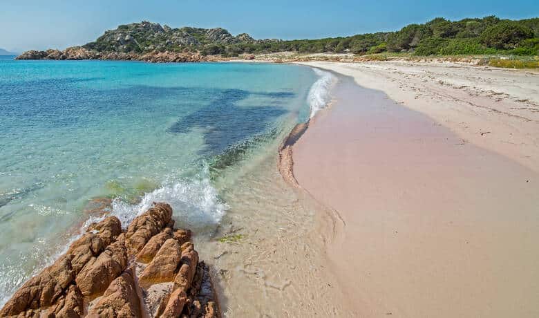Der leere rosa Strand auf Sardinien. Der Punkt, wo Wasser und Sand aufeinander treffen, leuchtet leicht rosa.