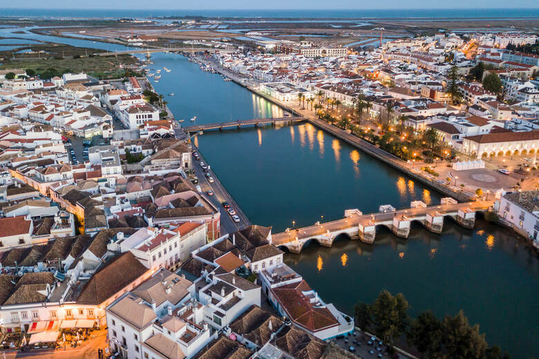 Luftaufnahme der Kleinstadt Tavira in der Dämmerung. Der Kanal mit seinen Brücken ist der Hauptfokus.