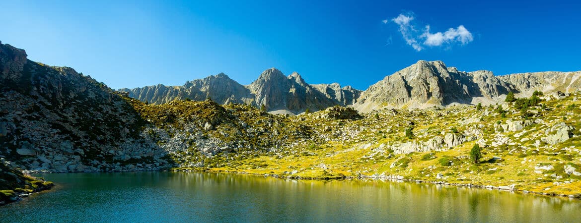 Ausblick auf einen Gebirgssee mit grüner Wiese und Bergen im Hintergrund, spanische Pyrenäen