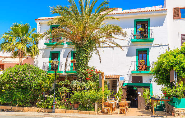 Ein traditionelles Haus mit Palmen, weißer Fassade und türkisen Rahmen in Sant Joan de Labritja