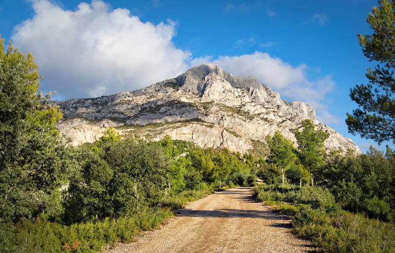 Schotterweg mit Blick auf das Gebirge Montagne Sainte-Victoire mit grüner Vegetation