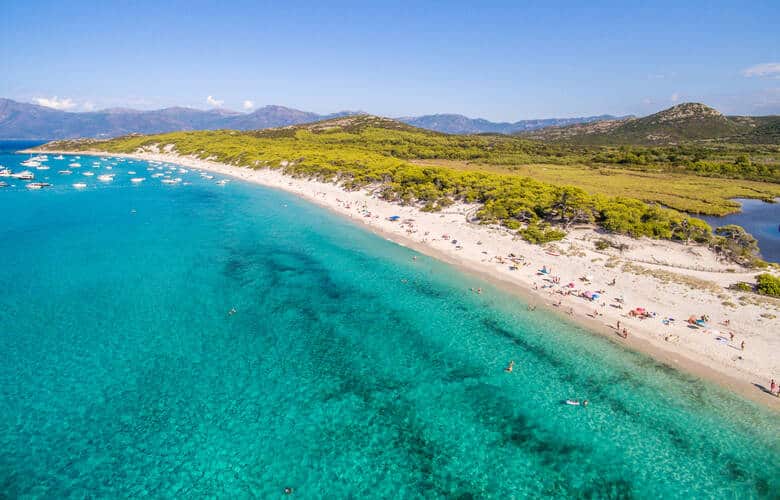 Der langezogene Strand Saleccia mit vielen Booten im Hintergrund