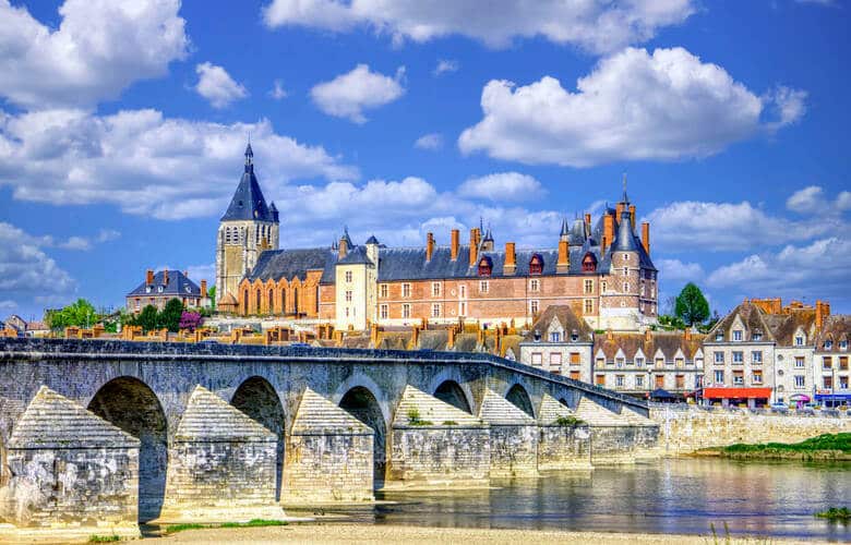 Schloss Gien mit rotem Stein und einer Brücke über die Loire im Vordergrund