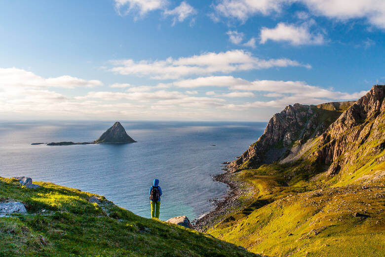Person geht in Norwegen wandern und blickt auf die Berge und das Meer